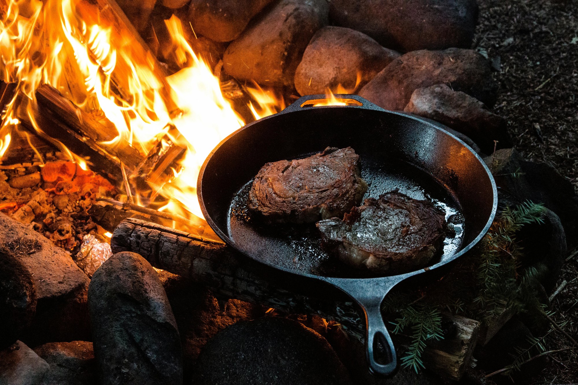 焚き火にかけた鋳鉄のフライパンでステーキを焼いている様子