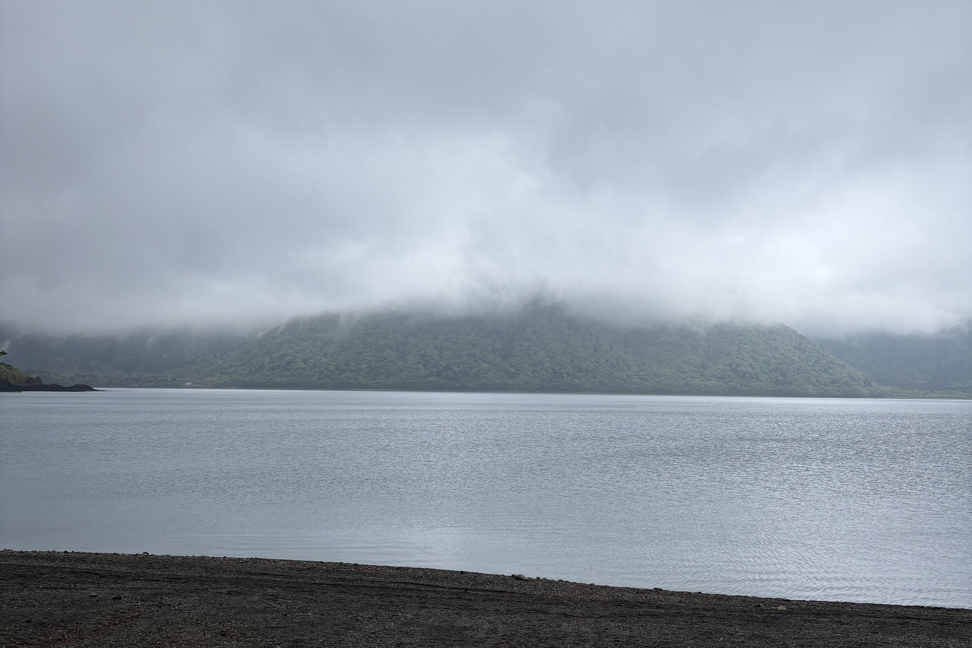 霧がかかった山と湖、暗い砂浜が広がる雨上がりのキャンプサイトの景色